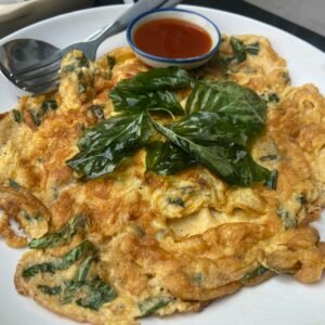 Thai-style spinach omelette with basil leaves served with spicy sauce on a white plate.